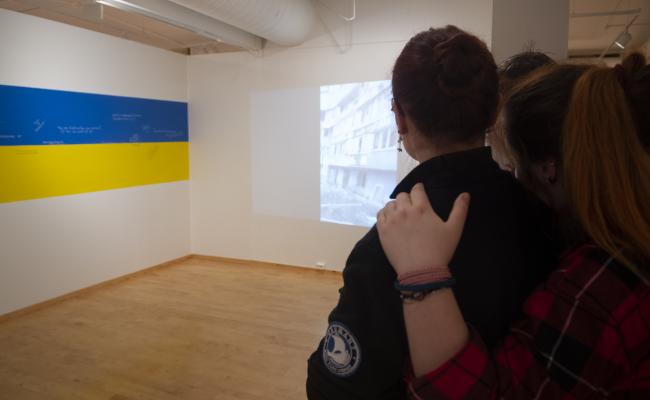 Julia Lytvynova og venene under utstillingsopninga i Longyearbyen. Ein projektor viser videoklipp frå krigssona. Julia Lytvynova og venene under utstillingsopninga i Longyearbyen.